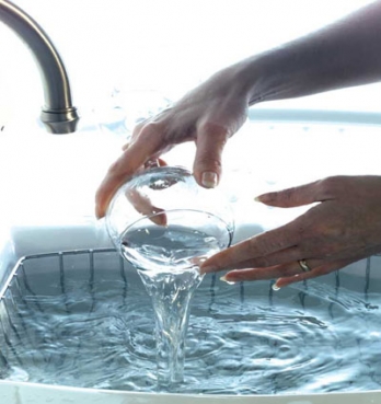 Rinsing a glass under a kitchen tap at a sink